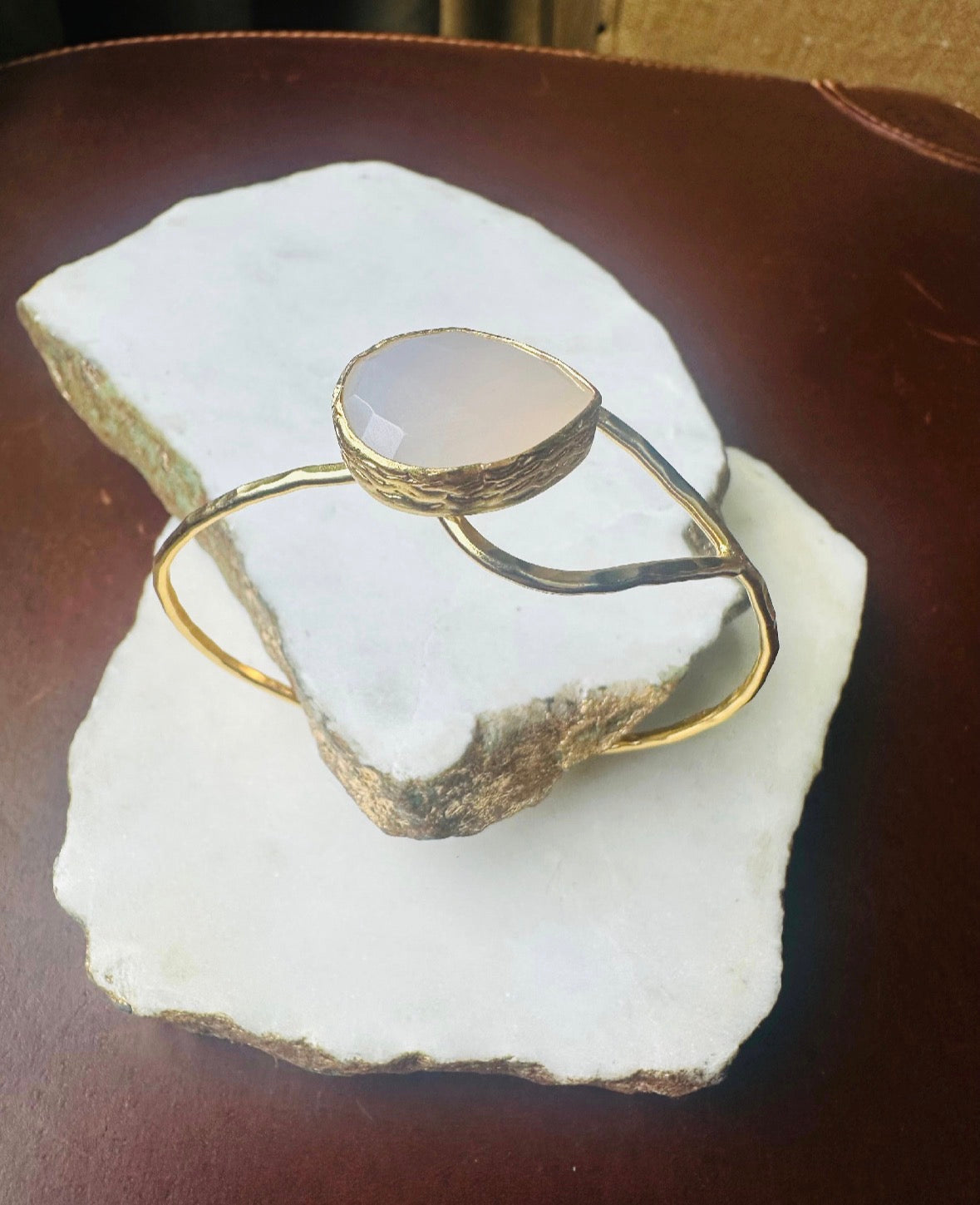 Gold-plated artisanal bracelet with snow Quartz stone on a white marble slab