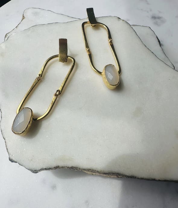 Contemporary Handmade sustainable Gold-plates earrings with snow Quartz stones placed stylistically on a marble surface