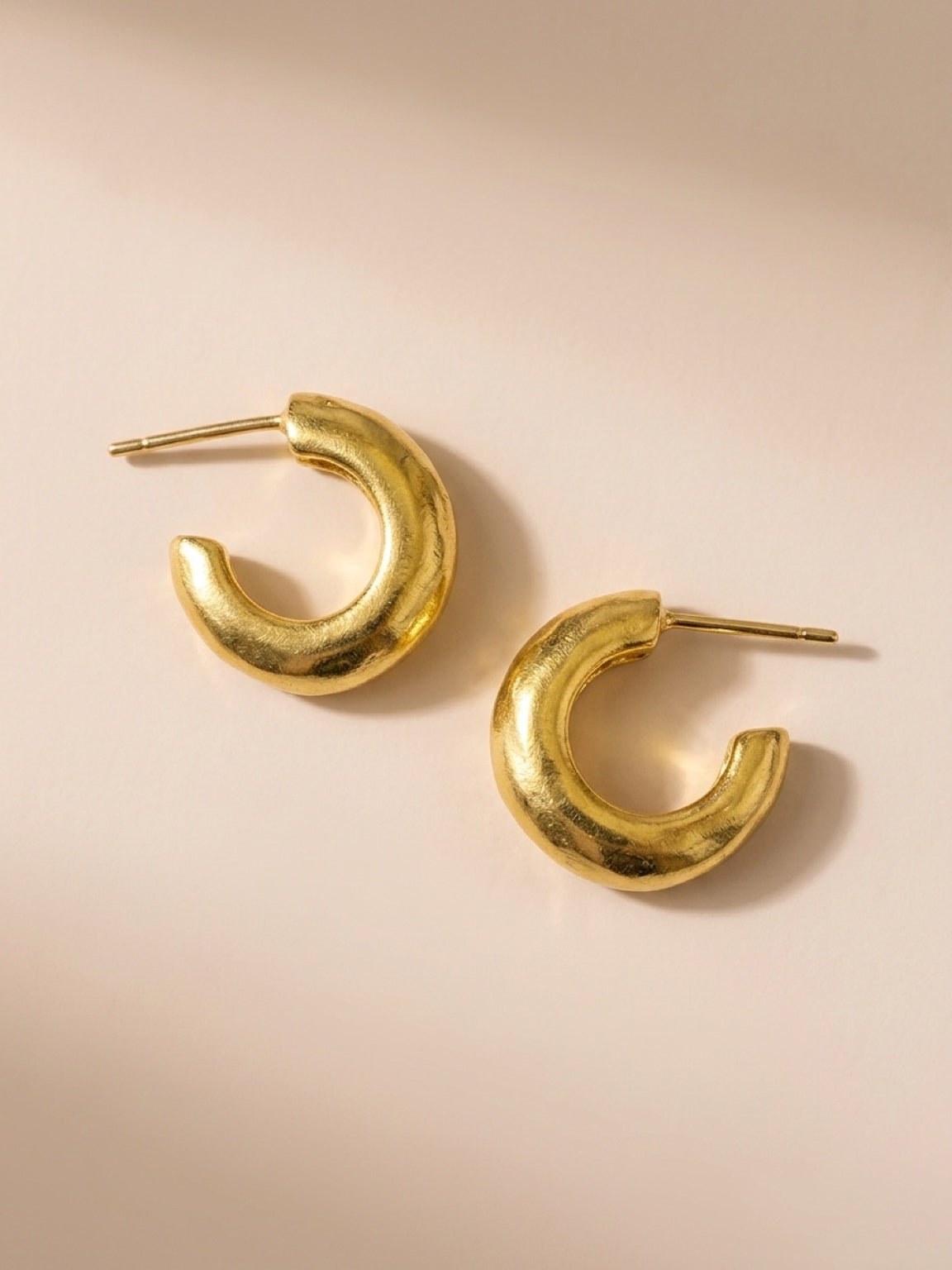 Handmade gold-plated Huggies laying on beige background