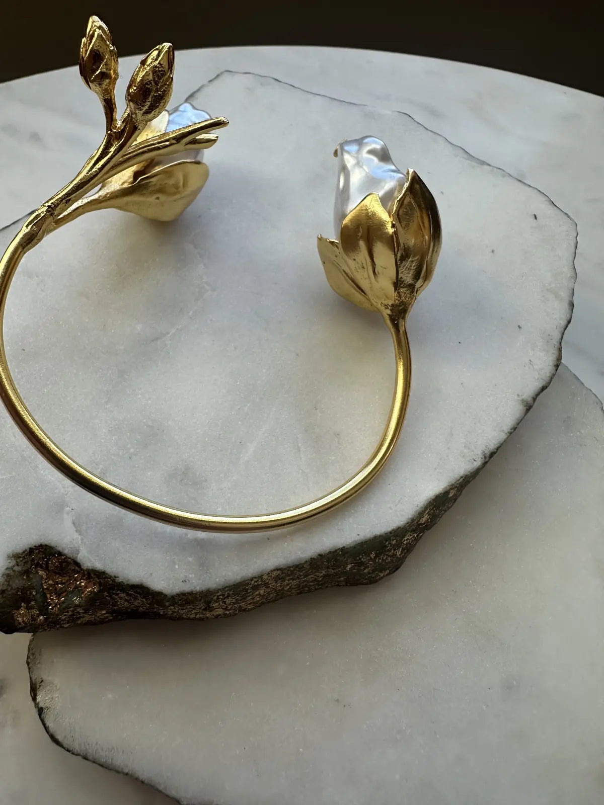 Gold-plated baroque pearl floral cuff bangle  on a marble surface facing right 