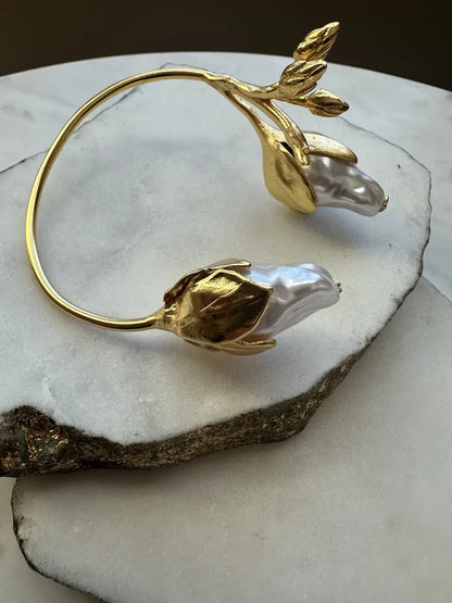 Gold-plated cuff bracelet with baroque pearls on a marble surface