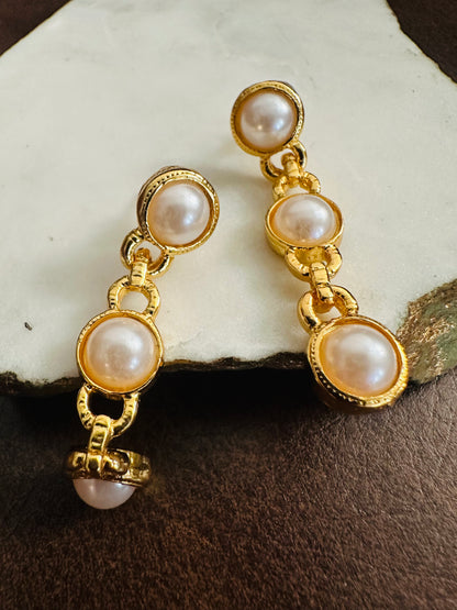 Gold earrings with pearl drops on a textured surface