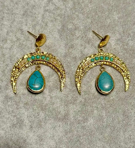 A pair of handmade gold-plated crescent-shaped drop earrings with small turquoise and pearl gemstones along the top arch and a larger teardrop turquoise stone hanging below, displayed on a textured gray background.
