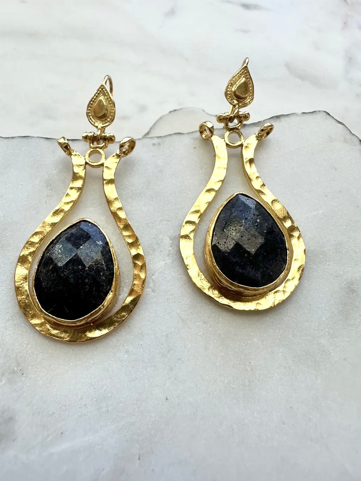 Gold earrings with lapis lazuli teardrop stones on a marble surface