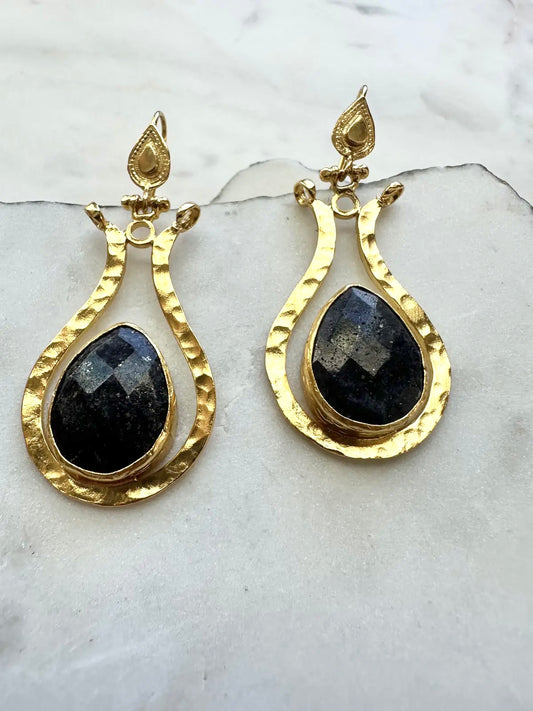 Gold earrings with lapis lazuli teardrop stones on a marble surface