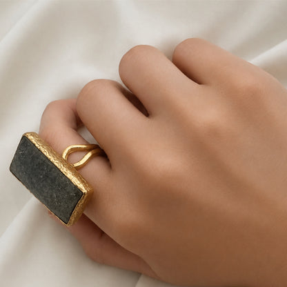 Close up of Hand wearing a gold ring with a dark gray lapis lazuli stone on a white fabric background
