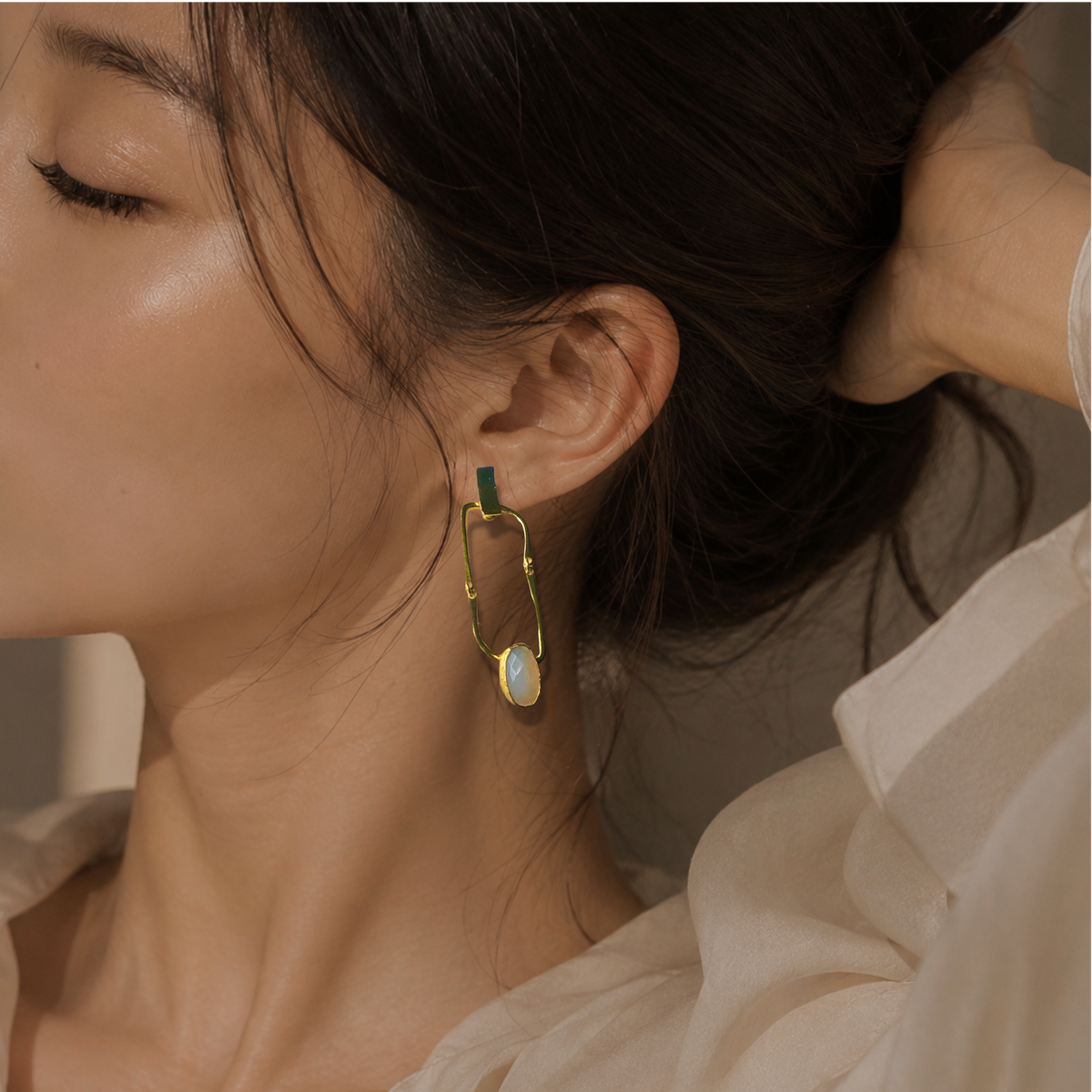 A close-up lifestyle shot of a woman wearing beige blouse and handmade gold plated snow Quartz earrings 