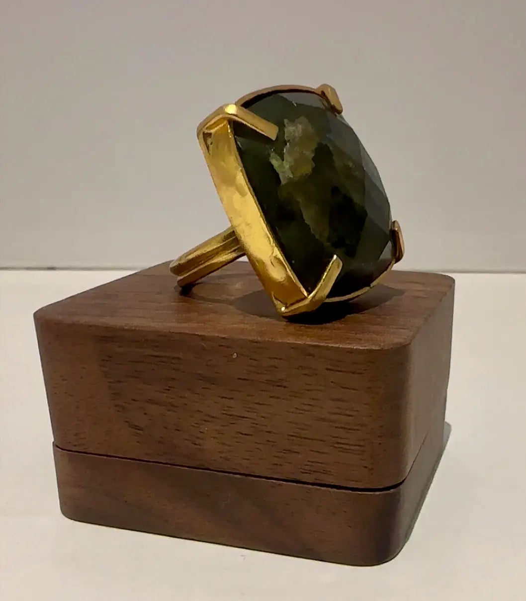Handmade Gold plated ring with a large labradorite gemstone on a wooden stand against a white background