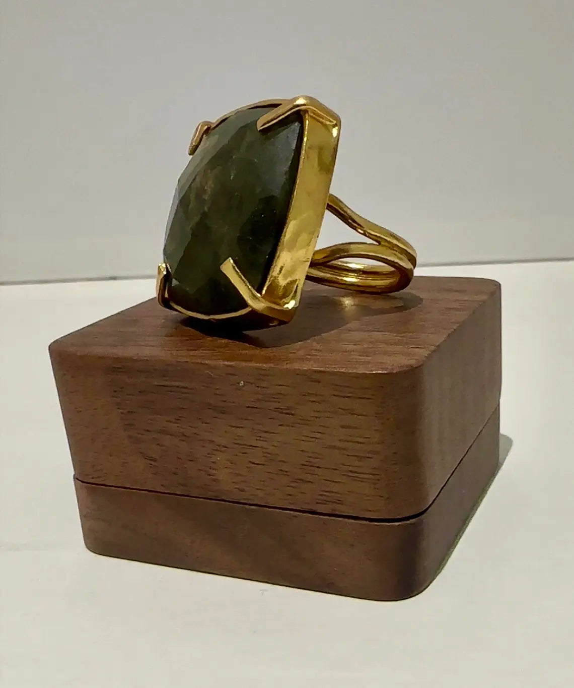 Goldplated waterproof ring with a large labradorite stone on a wooden stand against a white background