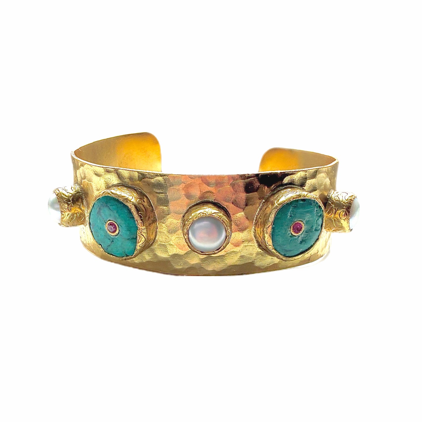 A handmade hammered gold cuff bracelet featuring turquoise inlay circles with small red zircon centers and white pearls shown on a white background