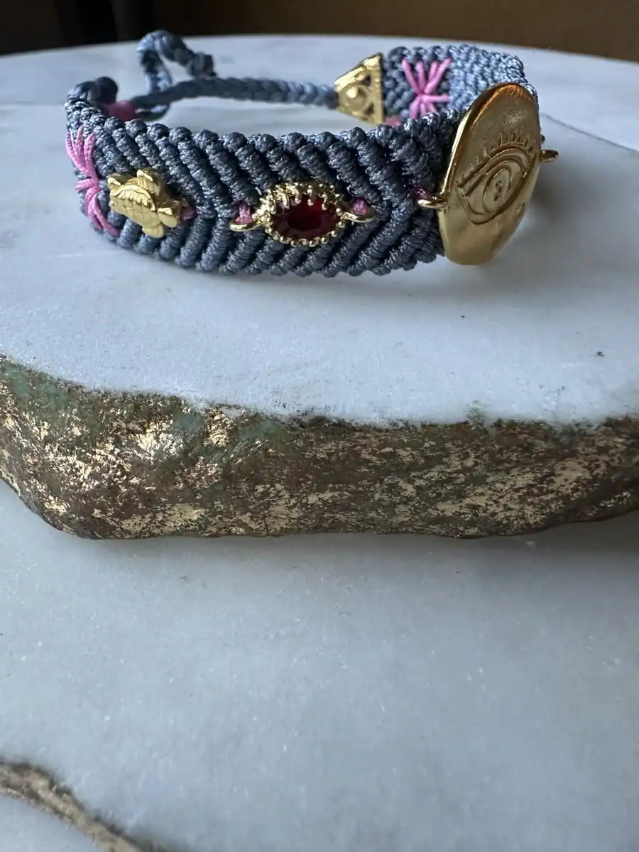 Slate gray handmade woven Bracelet with gold-plated evil eye charm and zircon crystals on a textured surface