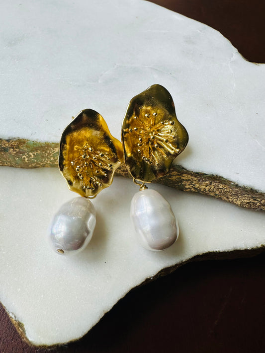 Gold and baroque pearl earrings on a white stone surface