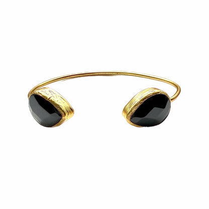 Handmade Gold-plated cuff bangle with two teardrop onyx gemstones on a white stone surface