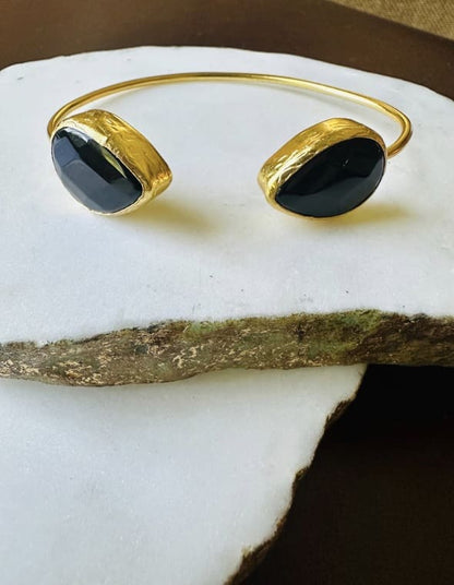 Handmade Gold-plated cuff bangle with two teardrop onyx stones on a white stone surface