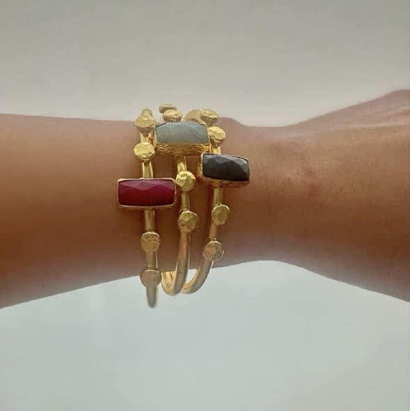 Stack of artisanal Gold-plated bracelets with colorful stones on a wrist against a neutral background