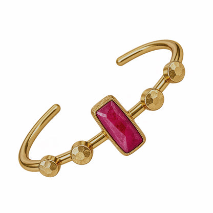 Gold cuff bracelet featuring a rectangular faceted ruby pink gemstone in the center and three textured gold ball accents on each side of the stone, set against a plain white background.