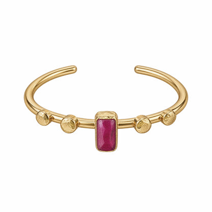A gold-plated cuff bracelet featuring a central rectangular ruby gemstone and four textured gold beads spaced along the band, set against a plain white background.