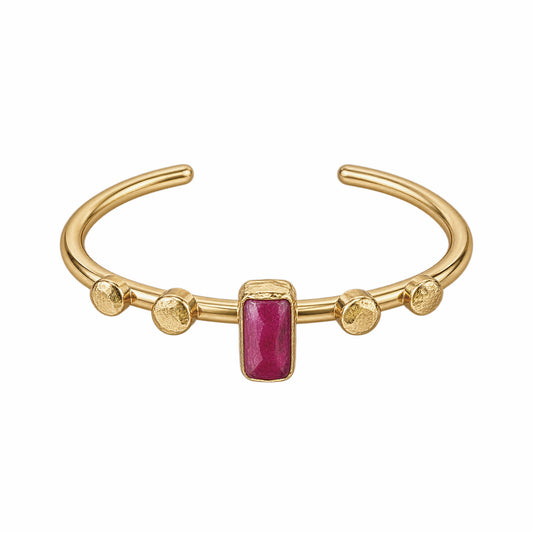 A gold-plated cuff bracelet featuring a central rectangular ruby gemstone and four textured gold beads spaced along the band, set against a plain white background.