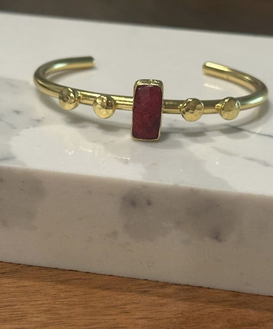 Handmade Gold-plated bangle with faceted ruby gemstone on a marble surface