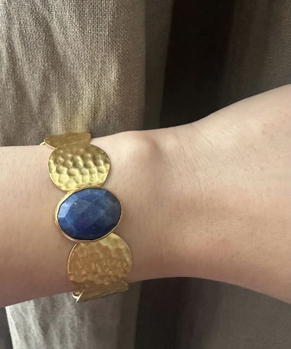 Gold-plated sustainable bracelet with a blue lapis lazuli gemstone on a wrist against a neutral background