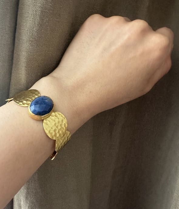 Gold-plated sustainable waterproof bangle with a blue lapis lazuli gemstone on a wrist against a brown background