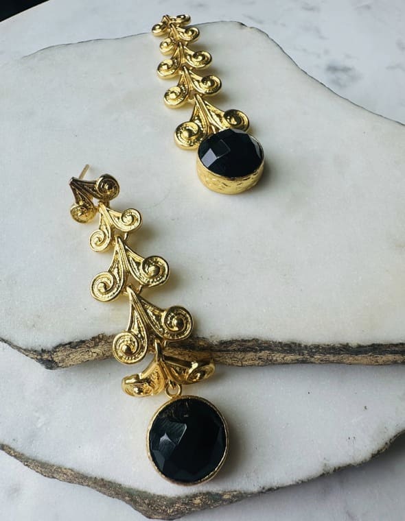 Handmade eco-friendly Gold-plated long dangle earrings with black onyx stone on a marble surface laying in diagonal formation 
