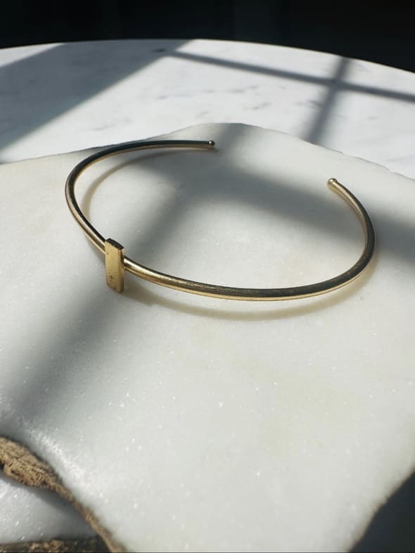 Gold-plated dainty stack bracelet on a marble white surface with natural light casting shadows.