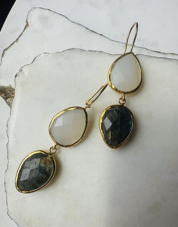 Artisanal eco-friendly  gold-plated teardrop labradorite and snow Quartz earrings diagonally placed on a white stone surface