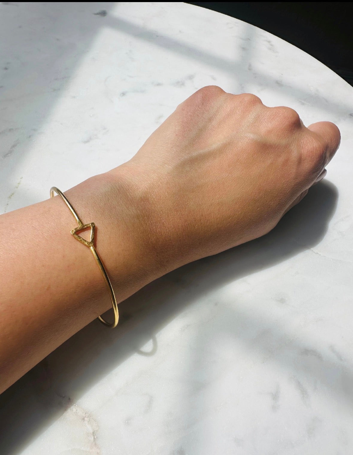 Gold-plated minimal bracelet on a wrist against a marble background