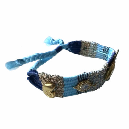 Turquoise, Blue and gold woven bracelet with gold plated fish charms, crystals, and beach resort charms on white surface