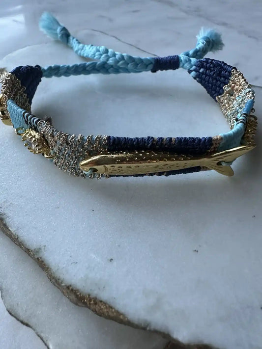 Turquoise, Blue and gold woven cord bracelet with gold plated fish charms, crystals, and beach resort charms on a white surface
