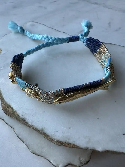 Blue, turquoise, and gold braided handmade woven bracelet with gold-plated fish charm and beach charms and crystals on a marble surface