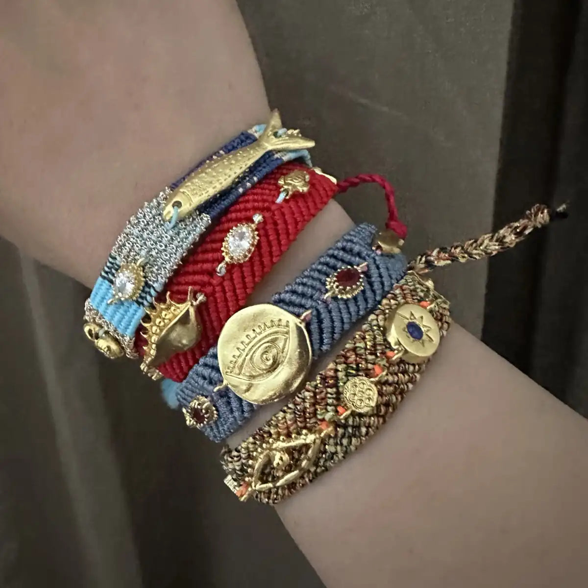 Close-up of a wrist wearing a stack of colorful woven bracelets with decorative gold-plated charms and zircon.
