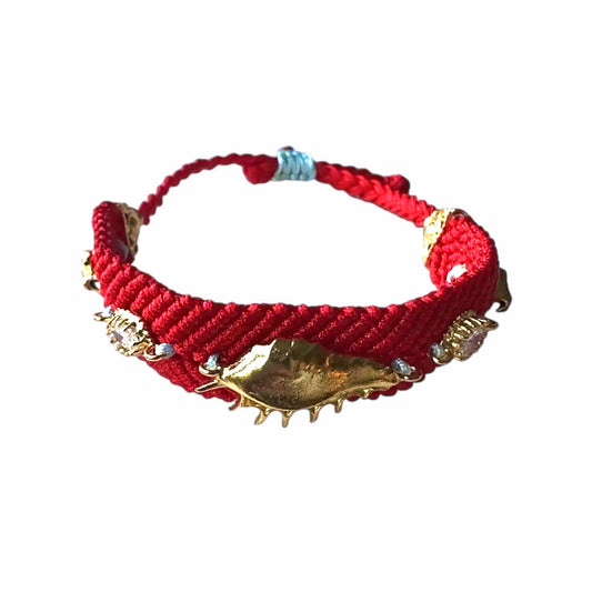 Handmade Red woven bracelet with gold-plated shell and evil eye accents on white surface
