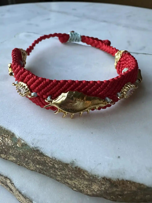 Red handmade woven braided bracelet with gold evil eye and beach accents and zircon on a marble surface