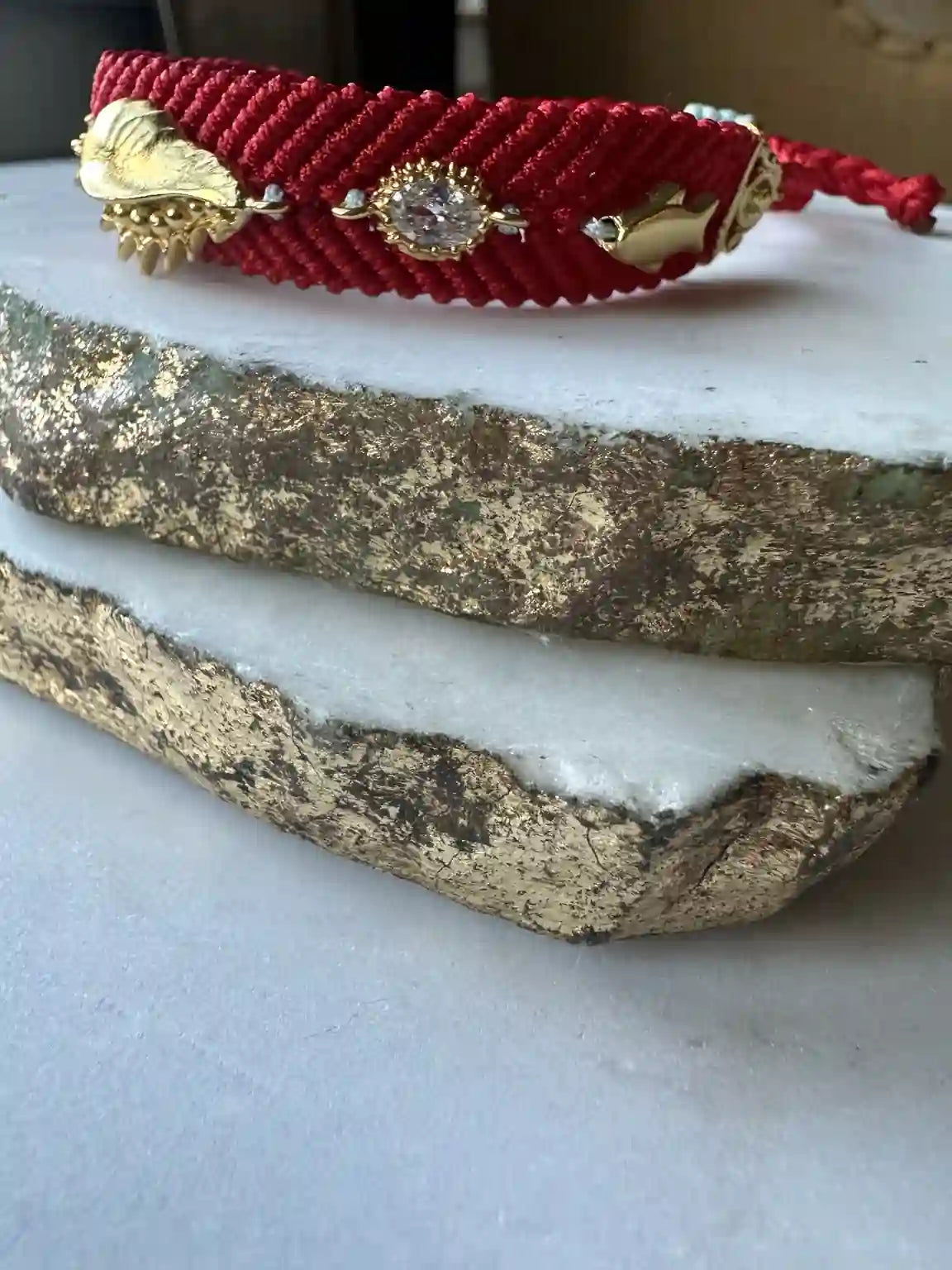 Handmade Red woven bracelet with gold-plated evil eye charm and beach charm on a marble surface