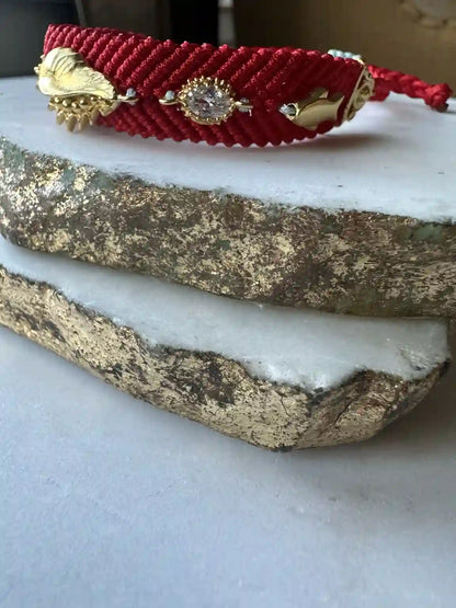 Handmade Red woven bracelet with gold-plated evil eye charm and beach charm on a marble surface