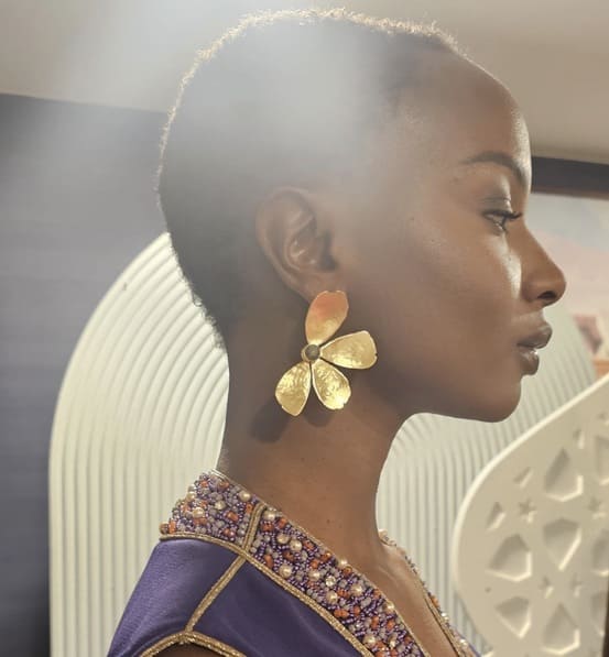 Model’s side profile wearing artisanal bold gold-plated flower earrings with pearl center 