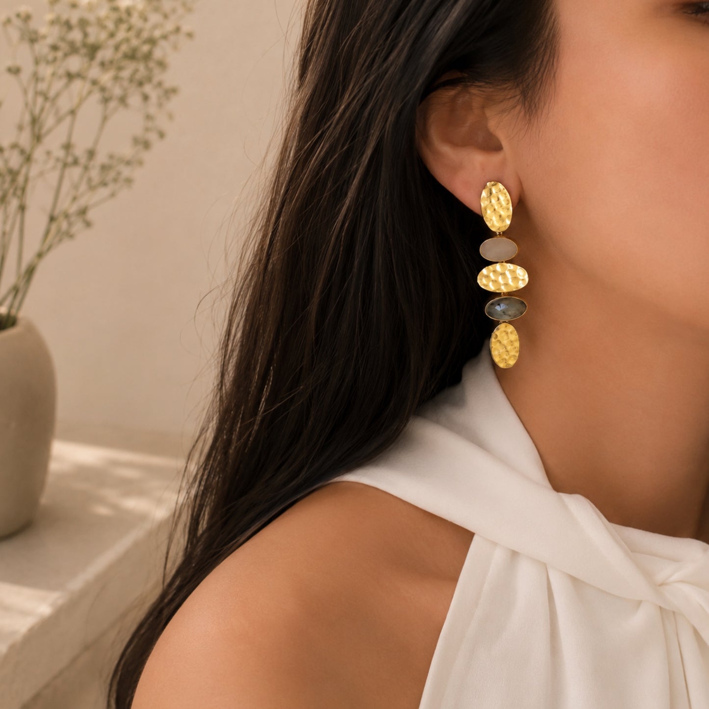 Lifestyle image close up of woman wearing handmade gold-plated snow Quartz and labradorite earrings with neutral background 