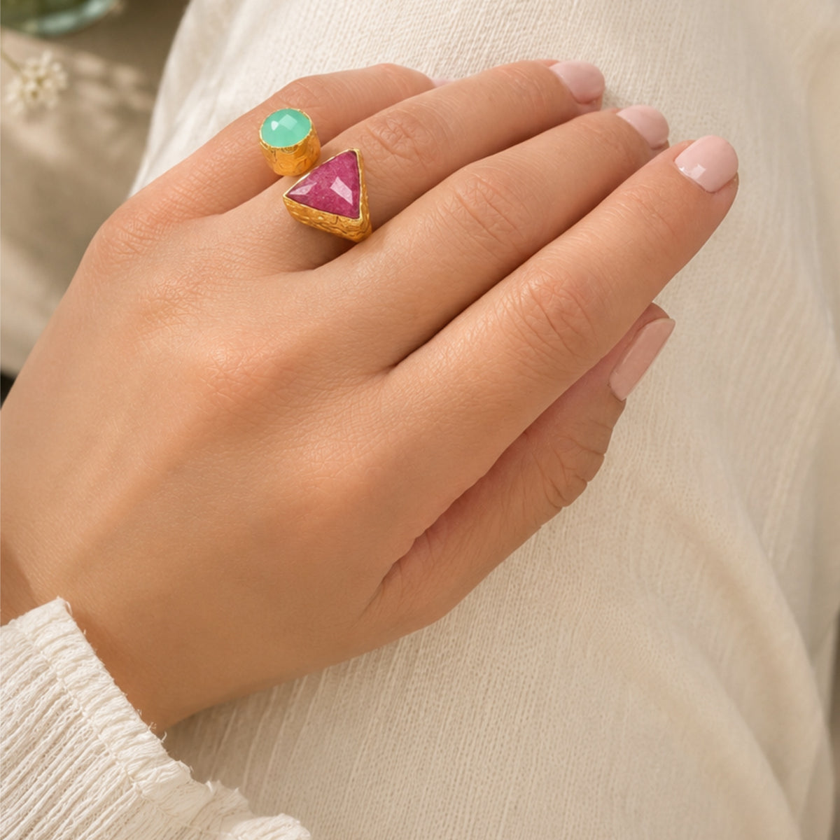 A close-up of a hand wearing multi-colored gemstone ring in Ruby and Aqua chalcedony against neutral backdrop 