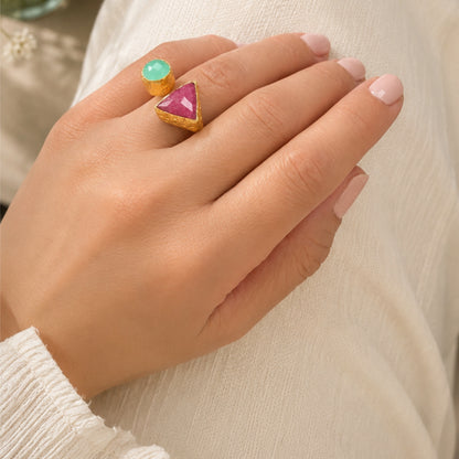 A close-up of a hand wearing multi-colored gemstone ring in Ruby and Aqua chalcedony against neutral backdrop 