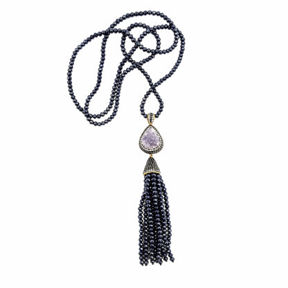 A long beaded Turkish necklace with dark navy blue beads, featuring a teardrop-shaped light purple druzy pendant surrounded by gold-toned metal, zircon, and a long multi-strand tassel hanging below.