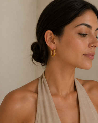 Model in beige suede halter top wearing textured gold-plated hoop earrings against a beige background 