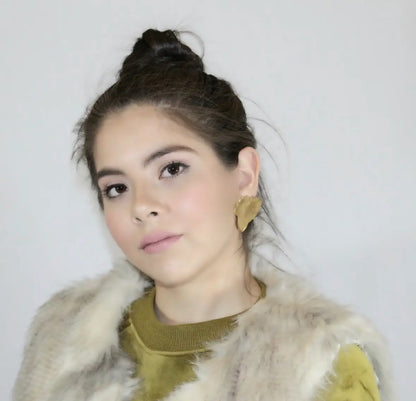 Model in green top and light gray fur vest wearing handmade gold-plated contemporary leaf stud earrings  