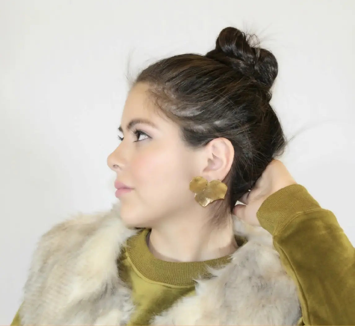 Model posing wearing green velvet top and light gray vest with contemporary handmade bold gold-plated leaf earrings 