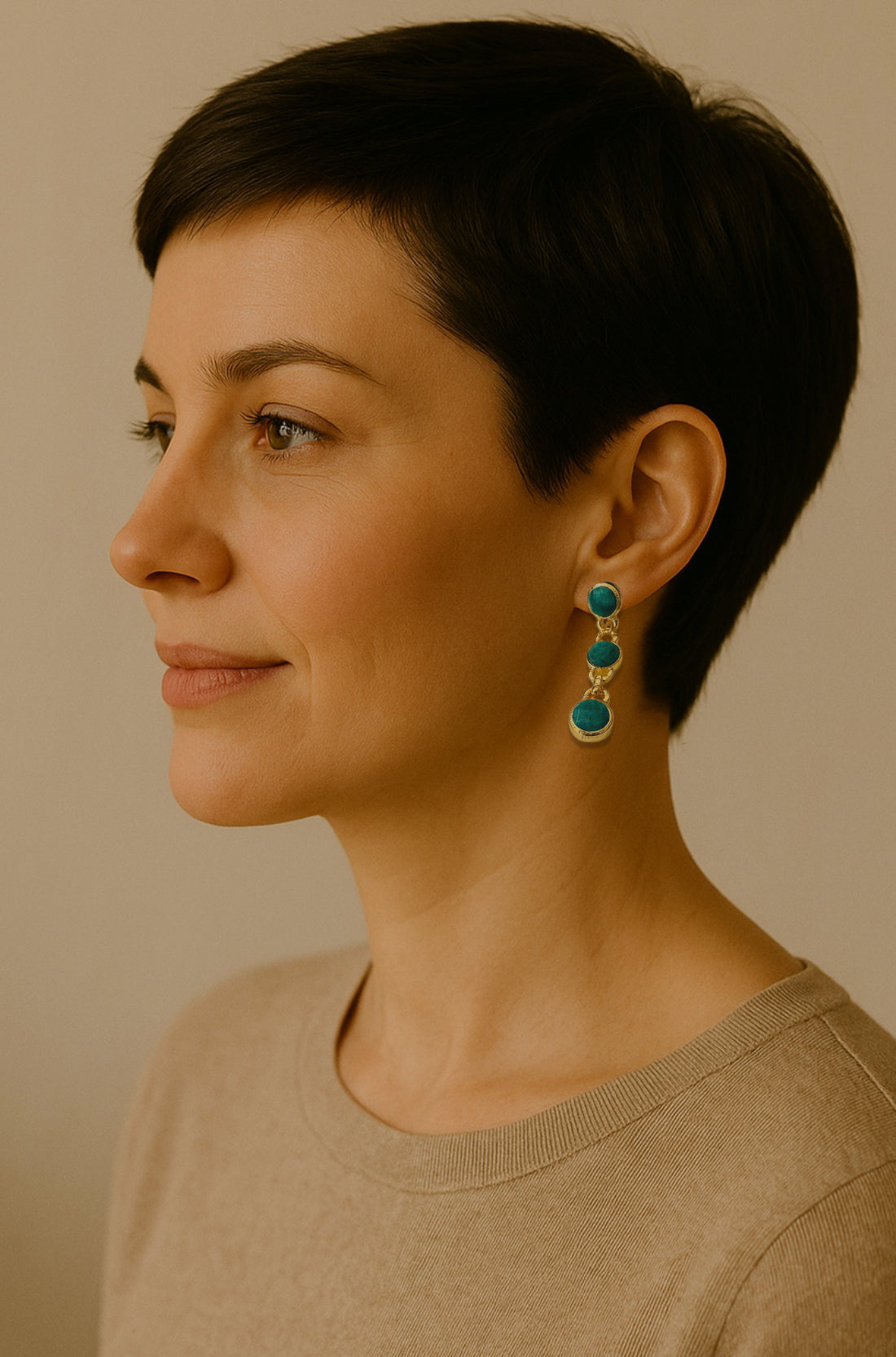 Woman wearing gold-plated handmade emerald dangle earrings against a neutral background