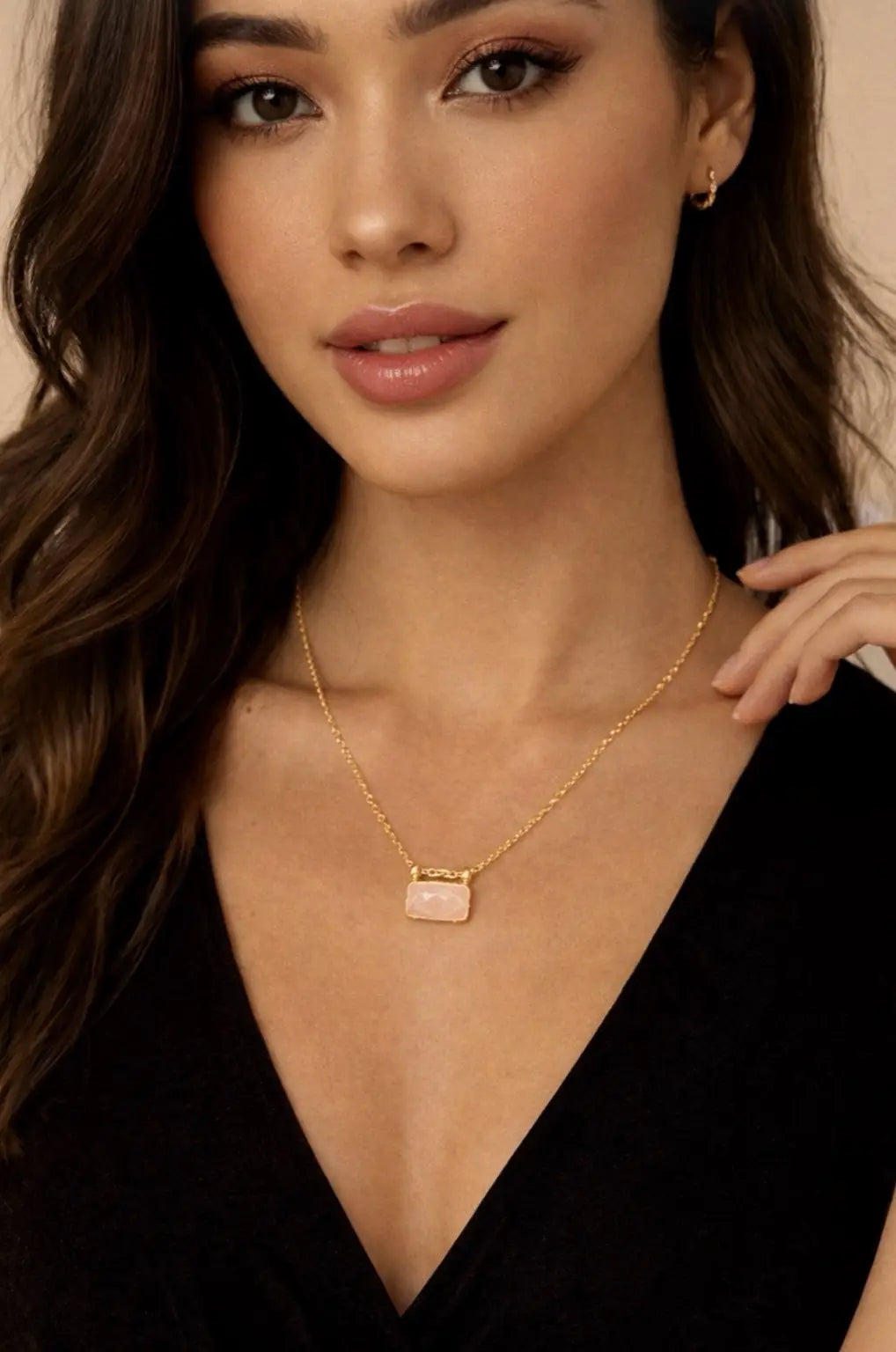 Female model wearing a gold-plated rose quart pendant necklace with a black top against a neutral background