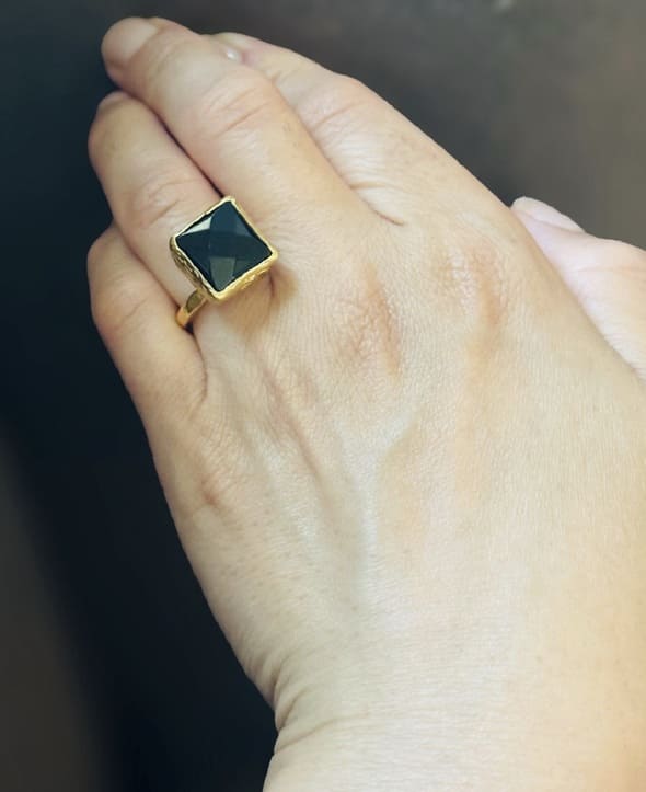Hand wearing artisanal sustainable gold-plated square onyx ring against brown background 