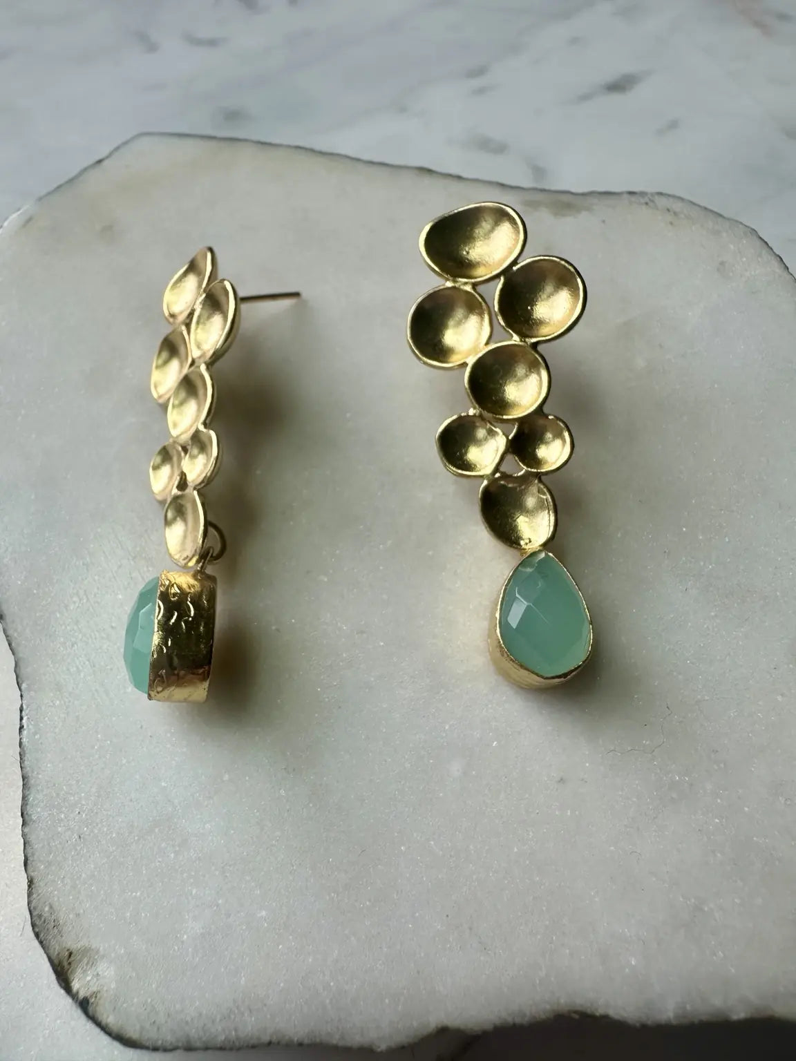A pair of gold-plated aqua chalcedony drop earrings displayed on a white stone slab with one facing the side 