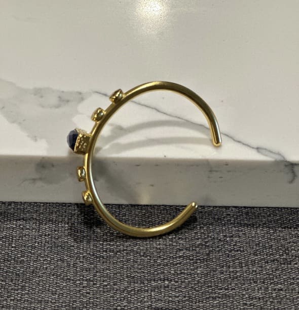 Side view of Handmade Gold-plated bangle with blue lapis lazuli gemstone on a marble surface